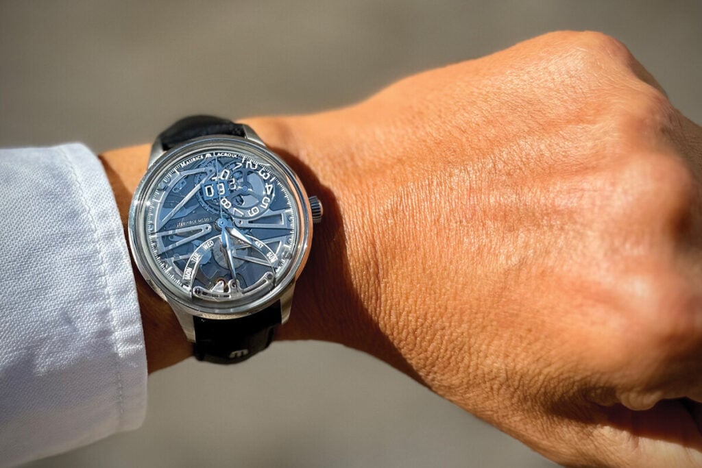 Rel&oacute;gio Maurice Lacroix com mostrador esquel&eacute;tico vis&iacute;vel no pulso de uma pessoa. O rel&oacute;gio est&aacute; em posi&ccedil;&atilde;o de destaque, com os detalhes das engrenagens, o n&uacute;mero 03 na data e os dias da semana vis&iacute;veis. A caixa de a&ccedil;o inoxid&aacute;vel e a pulseira de couro preto complementam o design elegante.