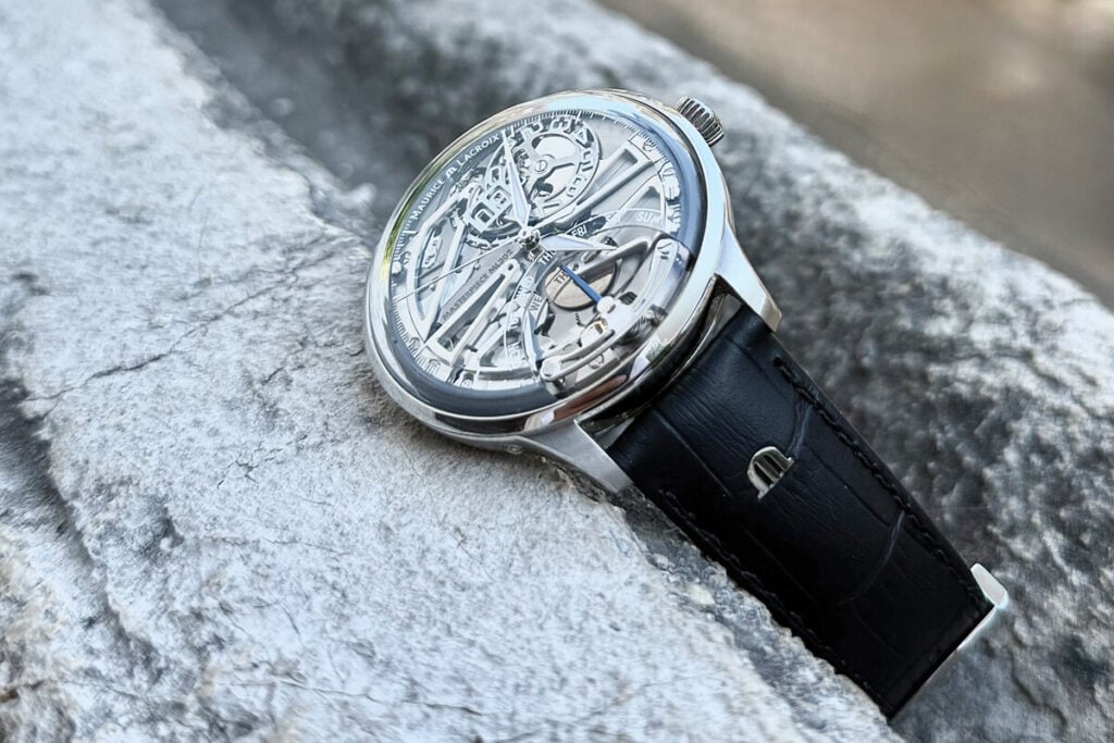 Rel&oacute;gio Maurice Lacroix com mostrador esquel&eacute;tico vis&iacute;vel, posicionado sobre uma superf&iacute;cie rochosa. A data "07" &eacute; exibida de forma destacada, e os dias da semana s&atilde;o vis&iacute;veis ao redor do mostrador. A caixa de a&ccedil;o inoxid&aacute;vel polido e a pulseira de couro preto complementam o design refinado.