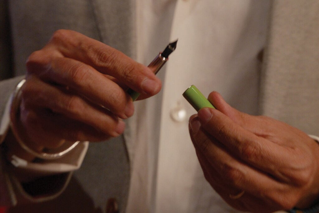 M&atilde;os de uma pessoa a segurar uma caneta estilogr&aacute;fica verde aberta, com a tampa numa m&atilde;o e o aparo vis&iacute;vel na outra.