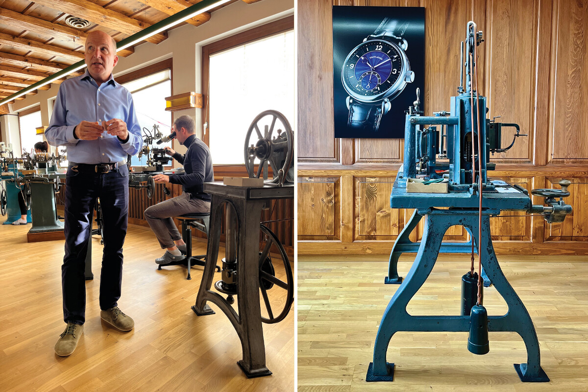 Oficina de relojoaria com técnico a trabalhar numa máquina e um homem em primeiro plano; ao lado, máquina industrial azul com cartaz de relógio na parede.