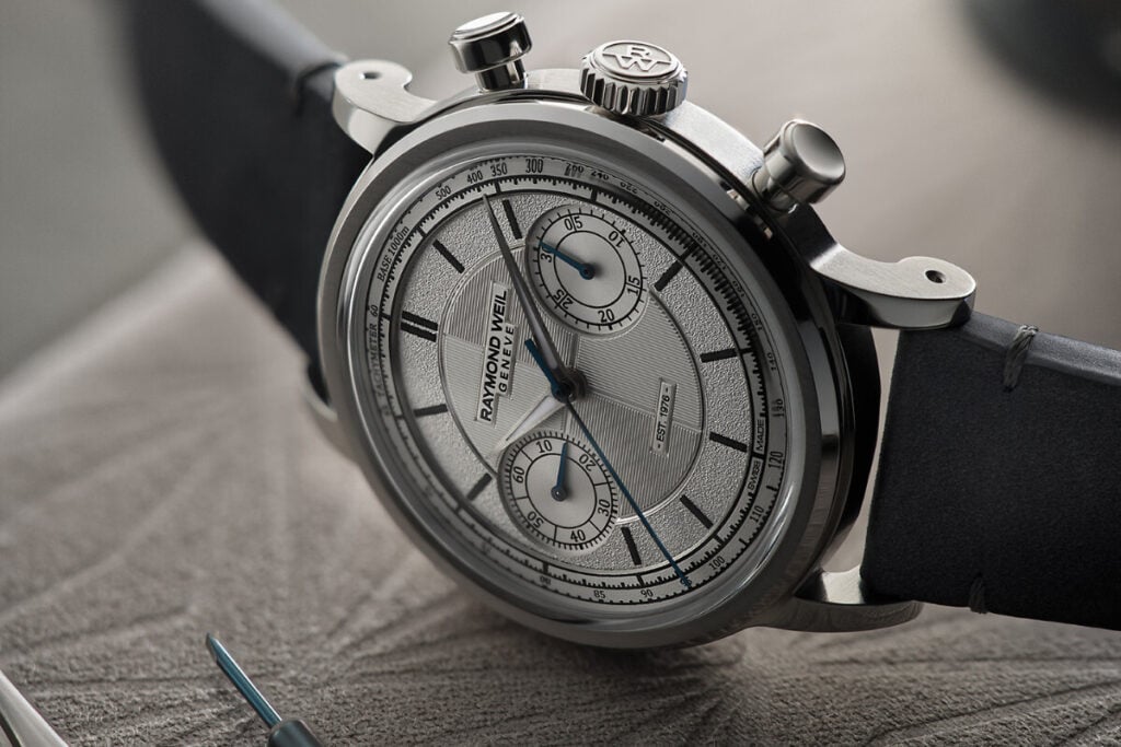 relógio de perfil na mesa: o comemorativo Raymond Weil The Fifty Chronograph com 37mm de diâmetro