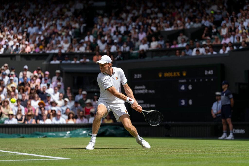 tenista Jannik Sinner em Wimbledon vestido de branco com court de relva | Foto: Rolex